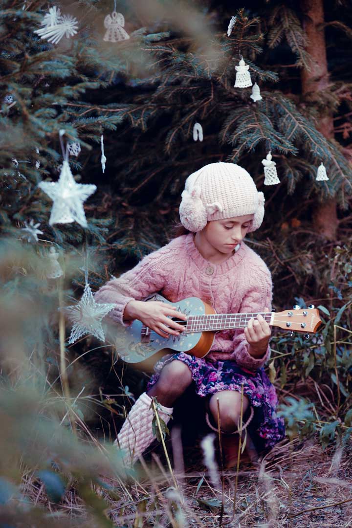 Dívka s ukulele při vánočním focení v ozdobeném lese