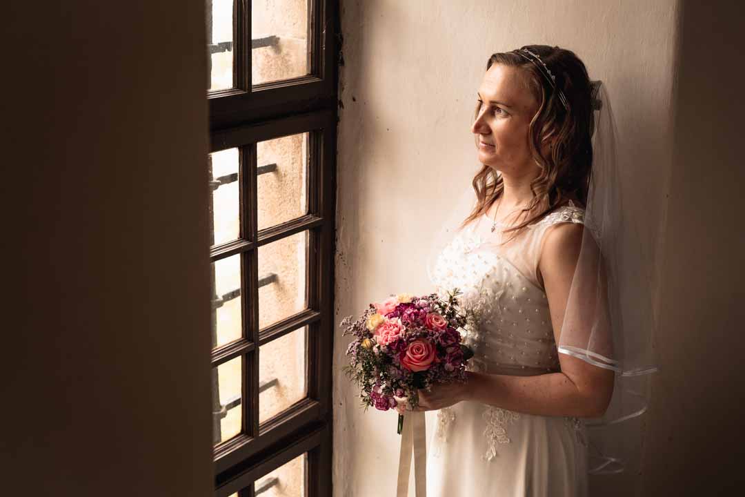 Nevěsta u okna při focení se svatebním fotografem