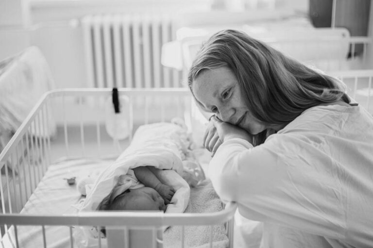Maminka s novorozenětem v postýlce v porodnici na pokoji